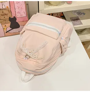 Close-up detail of a light pink student backpack featuring lace and pearl bow decorations.