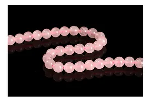 Macro view of natural pink rose quartz round beads arranged on a black reflective surface