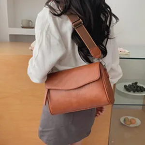 Back view of woman wearing a stylish brown leather crossbody bag with wide strap