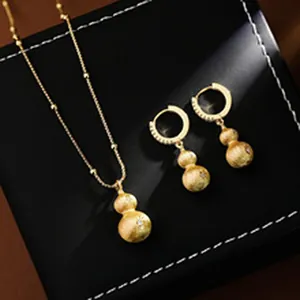 Close-up of golden gourd necklace and hoop earrings set on black jewelry box