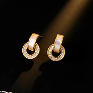Macro view of elegant C-shaped gold earrings with white inlay and sparkling crystals.