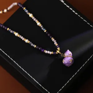 Macro detail of a beaded necklace with a purple gourd pendant and elegant pearls