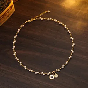 Detailed view of a delicate pearl necklace with a gold chain and evil eye pendant charms.