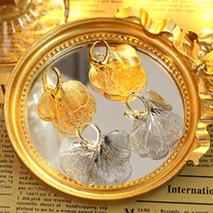 Close-up of pleated metal C-shaped hoop earrings in gold and silver shown on a mirror.