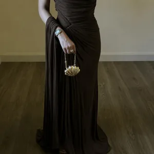 Detailed view of coffee brown pleated evening gown featuring elegant drapes and shell clutch