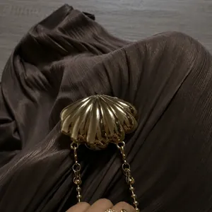 Detail shot of a polished golden shell ornament on a brown pleated evening dress