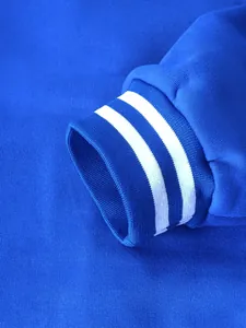 Close-up view of a blue baseball jacket sleeve cuff featuring white double-stripe ribbing