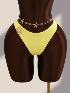 Gros plan du bas de bikini jaune avec chaîne de taille étoile de mer et accessoire broche soleil.