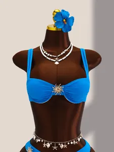 Détail du haut de bikini bleu avec ornement soleil doré sur un mannequin brun.
