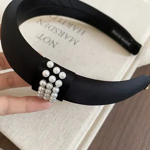 Close-up of elegant black satin padded headband with pearl accents and handmade label.