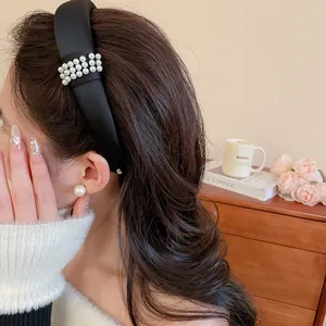 Detailed view of elegant black fabric headband with rows of pearl embellishments on model.