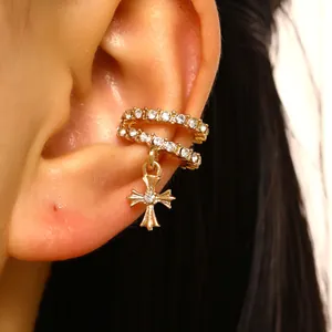 Macro view of a gold-plated ear cuff with cubic zirconia and a dangling cross charm