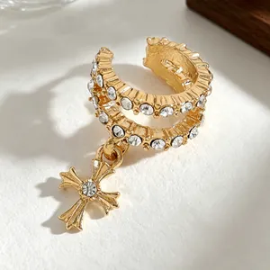 Close-up of gold cross ear cuff with sparkling zircon inlays on textured surface.
