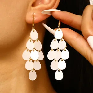 Détail des boucles d'oreilles à pampilles en acrylique blanc portées sur l'oreille