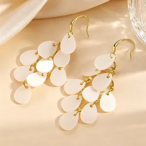 Gros plan d'élégantes boucles d'oreilles à pompons en pétales d'acrylique blanc et or