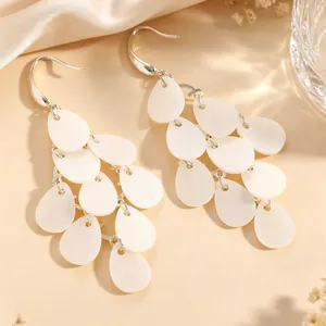 Gros plan sur d'élégantes boucles d'oreilles en pétales d'acrylique blanc avec pompon multicouche.