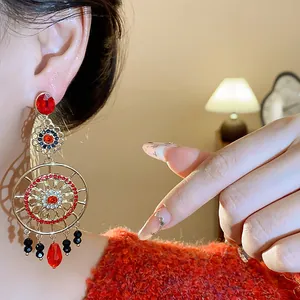 Détail de boucles d'oreilles ethniques avec strass rouges et fleurs dorées évidées.