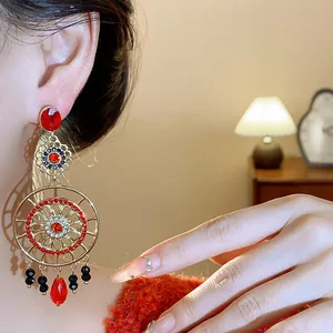 Détail macro de boucles d'oreilles fleurs ajourées vintage avec strass rouges et perles.