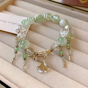 Nahaufnahme eines hellgrünen Glasperlenarmbands mit silbernen Schmetterlings- und Ginkgoanhängern.