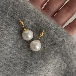 Elegant minimalist round white pearl stud earrings with gold posts on gray knit fabric