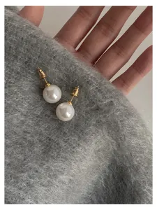 Detailed macro shot of elegant round pearl stud earrings with a gold finish on grey fabric.