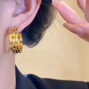 Detail view of a gold-plated link hoop earring featuring a luxury brick texture design