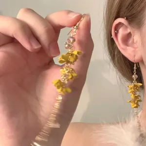 Splendidi orecchini a nappa con fiori gialli e zirconi, mostrati indossati e tenuti.