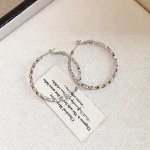 Macro detail of silver-toned geometric diamond-textured hoop earrings on jewelry card