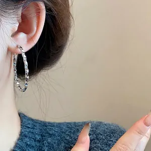 Detailed view of large silver-tone hoop earrings with geometric diamond texture on model