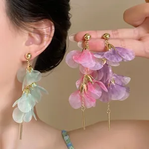 Detail of elegant pink and purple flower petal earrings with hanging long gold tassels.