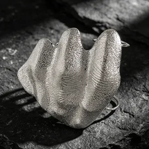 Close-up macro detail of a silver artistic irregular pleated joint ring on a dark rock