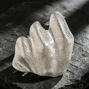 Close-up of an artistic irregular pleated silver joint ring with a textured metallic finish