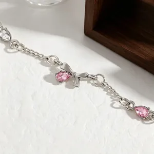 Close-up of silver-toned bow bracelet with pink teardrop zircons on white texture