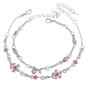 Close-up of two dainty silver bracelets with pink rhinestone flower and bow charms.