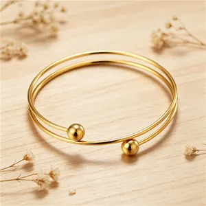 Detailed macro view of minimalist double-loop stainless steel gold bracelet with metal spheres