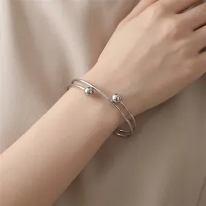 Close-up of a minimalist stainless steel double-loop bangle with bead accents on a wrist