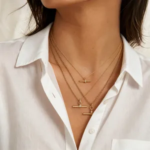 Detail view of three layered gold T-bar necklaces on a model wearing a white shirt