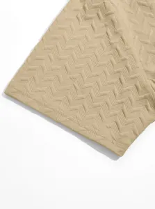 Close-up view of beige jacquard fabric with textured chevron pattern and stitched hem detail.