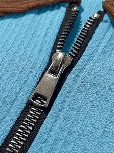 Close-up of metal zipper on blue waffle knit polo shirt showing fabric texture.