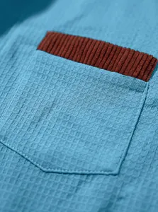 Macro detail shot of blue waffle-knit fabric with a brown corduroy pocket trim detail
