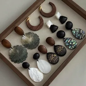 Detailed close-up view of various handcrafted wooden and shell earrings in a display tray