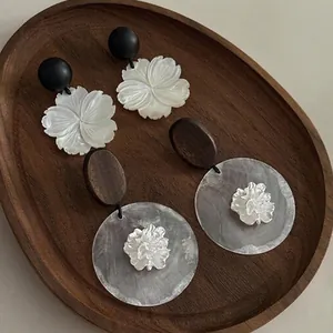 Detail of handcrafted floral earrings with shell texture and wooden accents on a tray