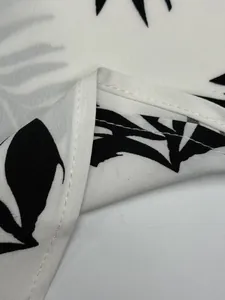Macro detail of high-quality stitching and tropical leaf print on white shirt fabric