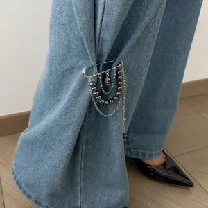 Vue détaillée d'une broche à chaîne à glands argentée portée comme clip sur un jean bleu.