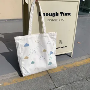 Detailed view of cream canvas tote bag featuring colorful embroidered cloud patterns