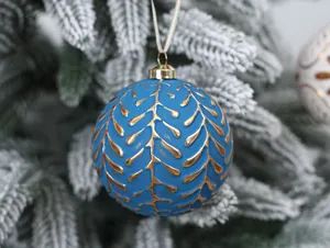 Detailed view of a blue Christmas ornament with gold leaf patterns on a snowy tree.
