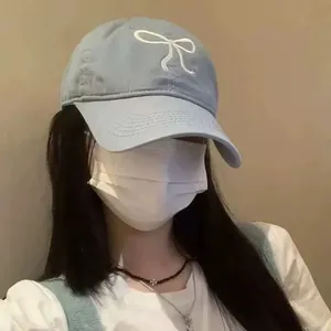 Stylish light blue baseball cap featuring a white bow embroidery worn by a female model