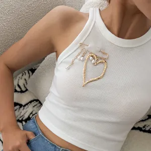 Fashionable chunky gold molten heart brooch featuring elegant pearl tassels on a white top.