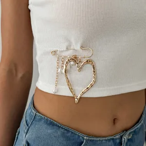 Close-up of a gold lava heart brooch with pearl tassels pinned on a white top.