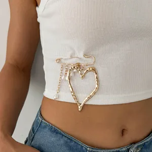 Detail of golden molten heart brooch with elegant pearl tassels on a white top.